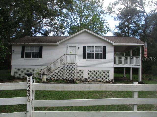 A white, elevated single-story house features a front porch, lattice skirting, and a wooden fence — 35236 REYNOLDS STREET, DADE CITY, FL