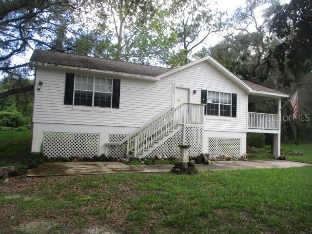 A white, elevated house with black shutters, a wooden staircase, and a covered porch — 35236 REYNOLDS STREET, DADE CITY, FL