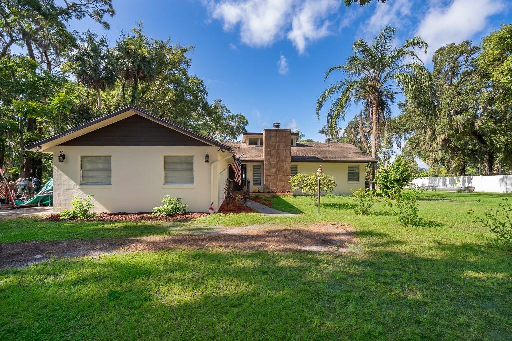 A single-story house with a stone chimney, light-colored stucco walls, and a large grassy yard — 1715 W LAKE MARY BOULEVARD, LAKE MARY, FL