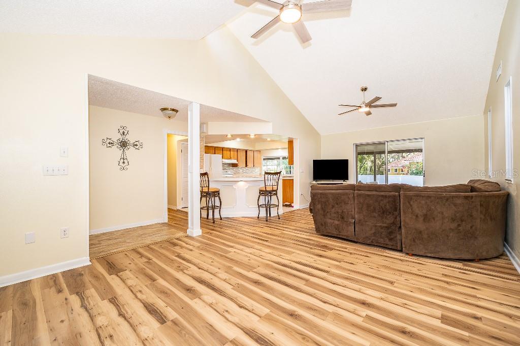 A living room with vaulted ceilings, wood-look flooring, and an open kitchen with bar seating — 1715 W LAKE MARY BOULEVARD, LAKE MARY, FL