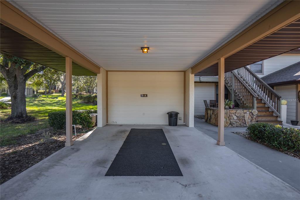 A covered carport features a concrete floor with a black mat and a wooden staircase — 240 E GLASSBORO COURT UNIT 4A, HERNANDO, FL
