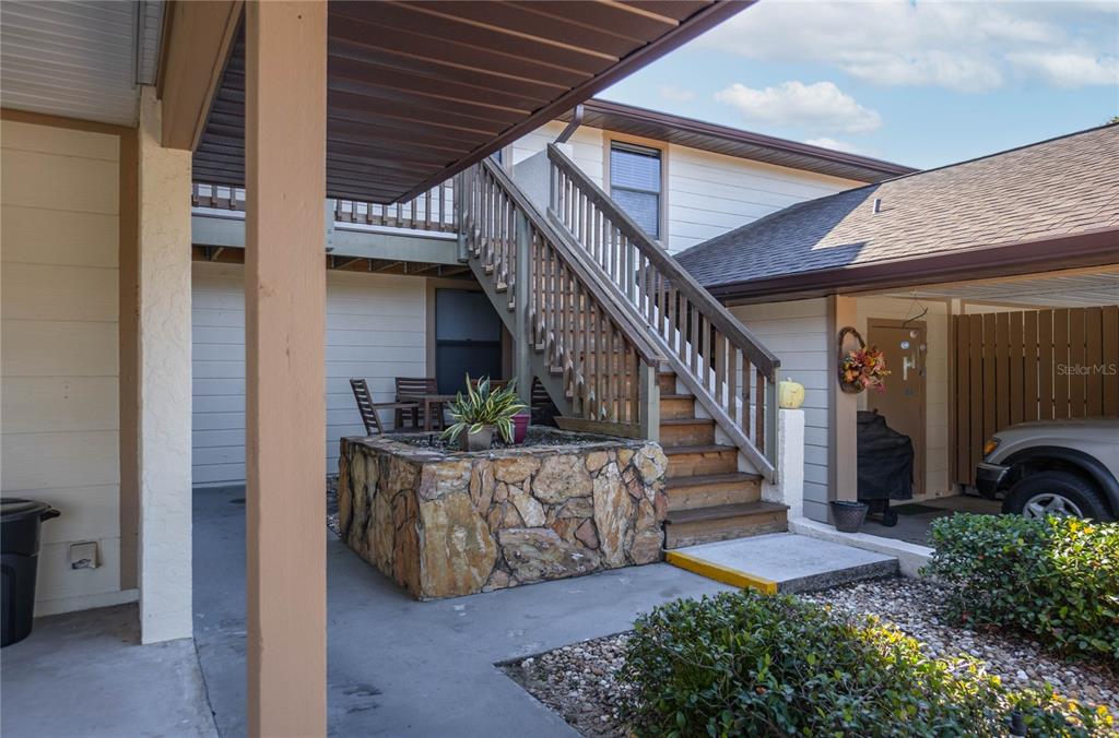 An exterior view of a building entrance featuring a stone planter and wooden staircase — 240 E GLASSBORO COURT UNIT 4A, HERNANDO, FL