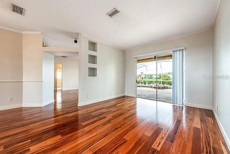 An empty living room features hardwood floors, built-in wall niches, and sliding glass doors to a pool — 2415 RAVEN CROFT COURT, ORLANDO, FL