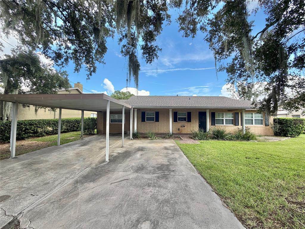 A single-story brick house features a large carport and a concrete driveway under oak trees — 4414 BONNET LAKE DRIVE, HAINES CITY, FL