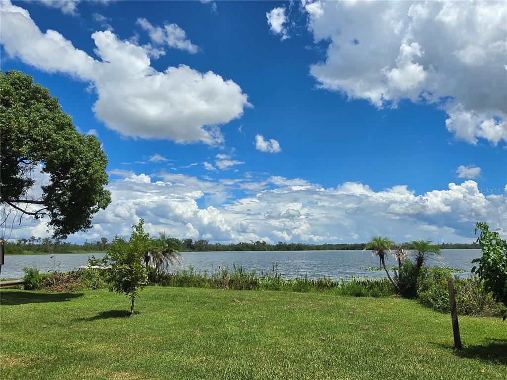 A grassy lawn leads to a lake under a bright blue sky with large clouds — 4414 BONNET LAKE DRIVE, HAINES CITY, FL