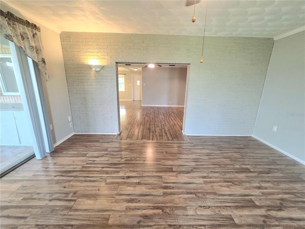 A living room with light-colored brick walls, wood-look flooring, and an open doorway to another room — 4414 BONNET LAKE DRIVE, HAINES CITY, FL