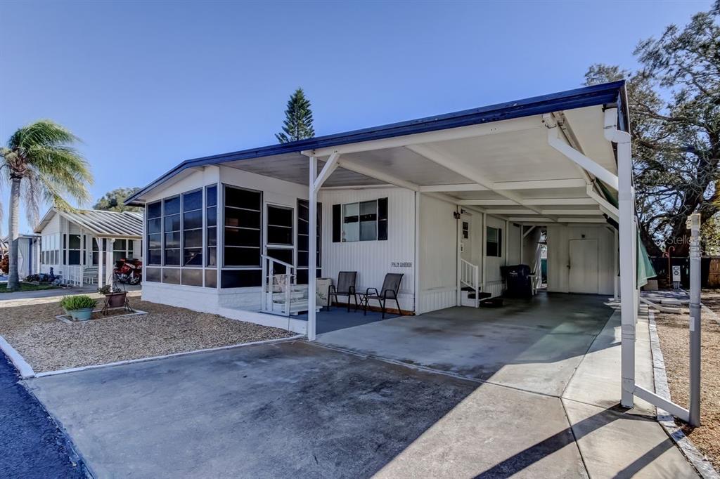 A single-story mobile home with a screened-in porch, carport, and gravel landscaping — 3430 TIKI DRIVE, HOLIDAY, FL