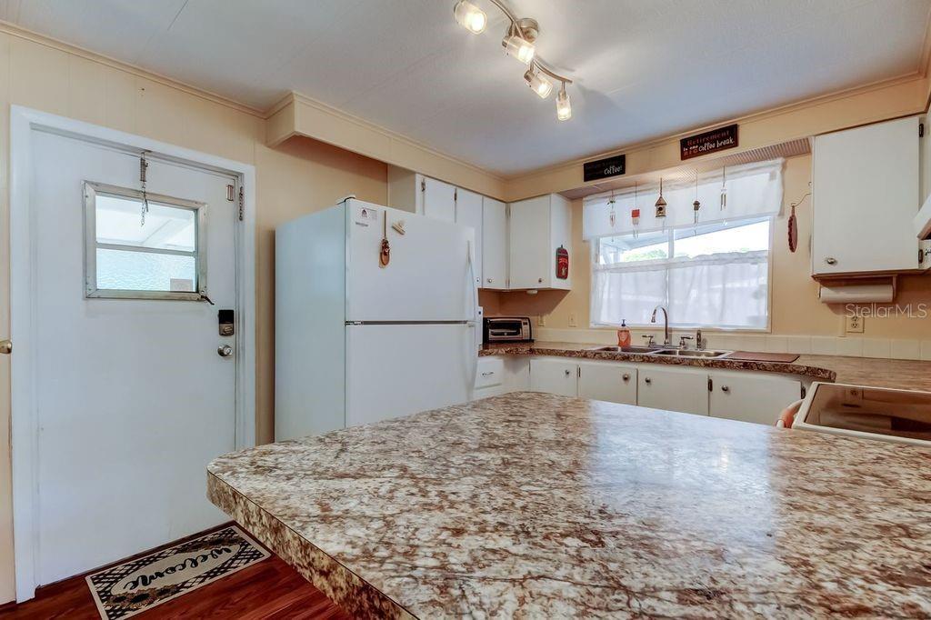 A kitchen features white cabinets, a granite-patterned island, and a white refrigerator — 3430 TIKI DRIVE, HOLIDAY, FL