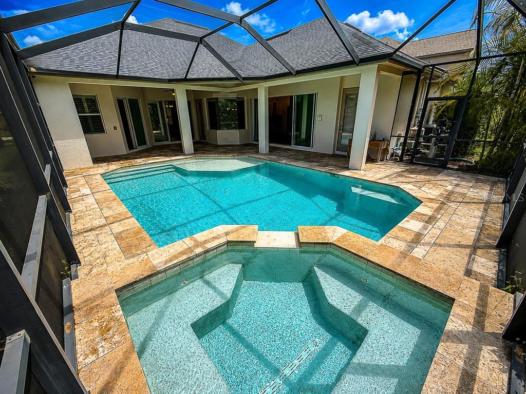 A screened-in patio features a swimming pool, a raised spa, and light-colored stone decking — 1637 ABYSS DRIVE, ODESSA, FL