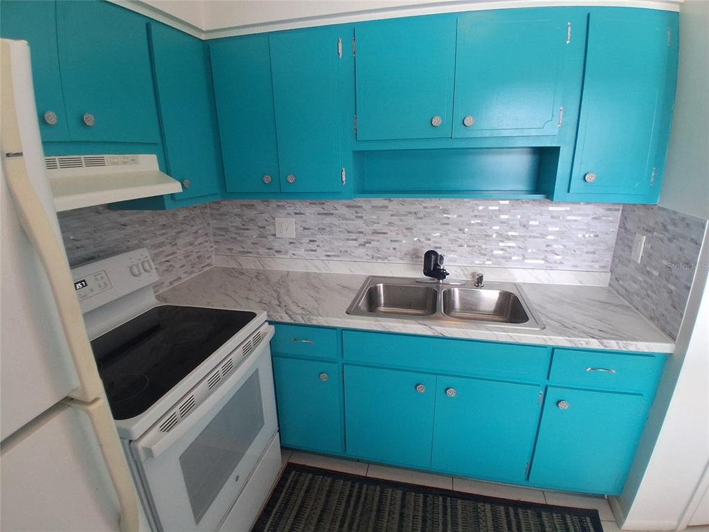 A kitchen features bright blue cabinets, a white stove, and a marble-patterned countertop — 125 PORTREE DRIVE, DUNEDIN, FL