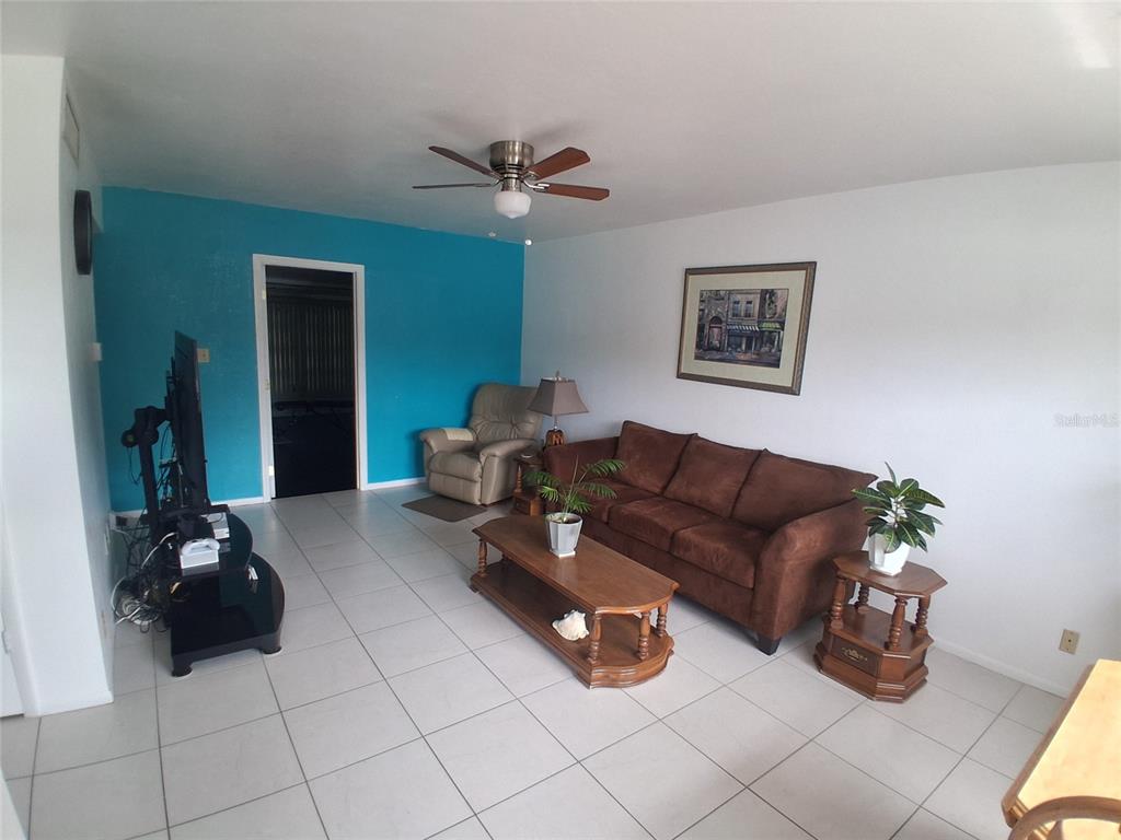 A living room features white tile floors, a brown sofa, and a bright blue accent wall — 125 PORTREE DRIVE, DUNEDIN, FL