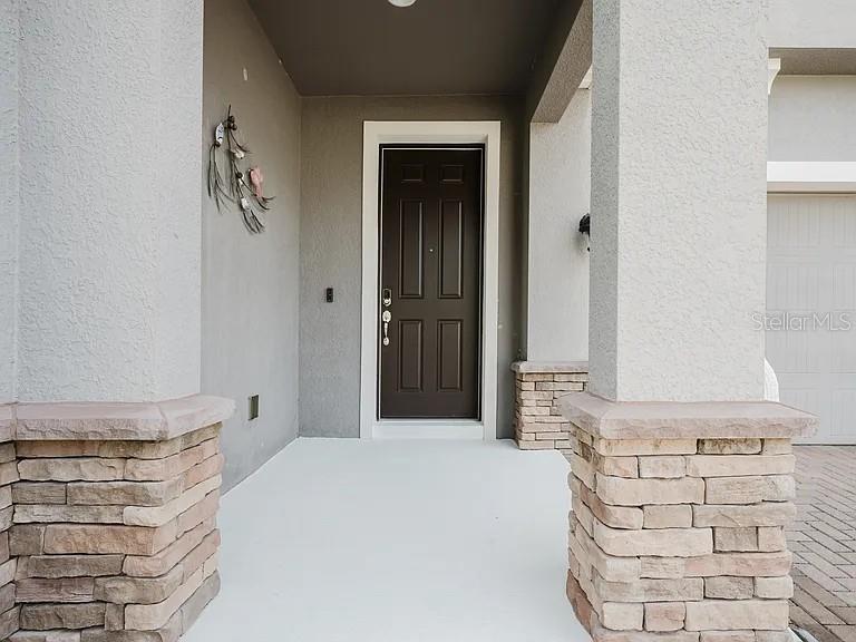 A covered entryway features a dark brown front door flanked by two stone-based stucco columns — 9072 OVERLOOK PASS DRIVE, WINDERMERE, FL