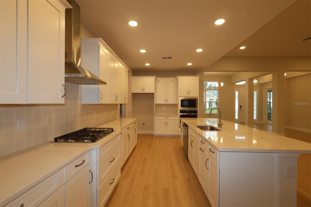 A kitchen under construction features white cabinets, a large island with blue protective film, and light wood flooring — 3223 ROSEVILLE DRIVE, APOPKA, FL