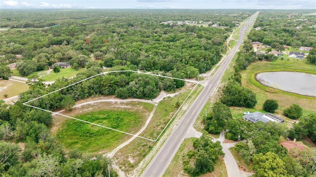 An aerial view shows a vacant, partially wooded lot outlined in white next to a road — COUNTY LINE ROAD, SPRING HILL, FL