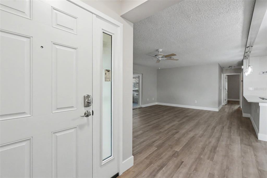 An empty living room features wood-look flooring, a ceiling fan, and sliding glass balcony doors — 1502 16TH CIRCLE SE, LARGO, FL