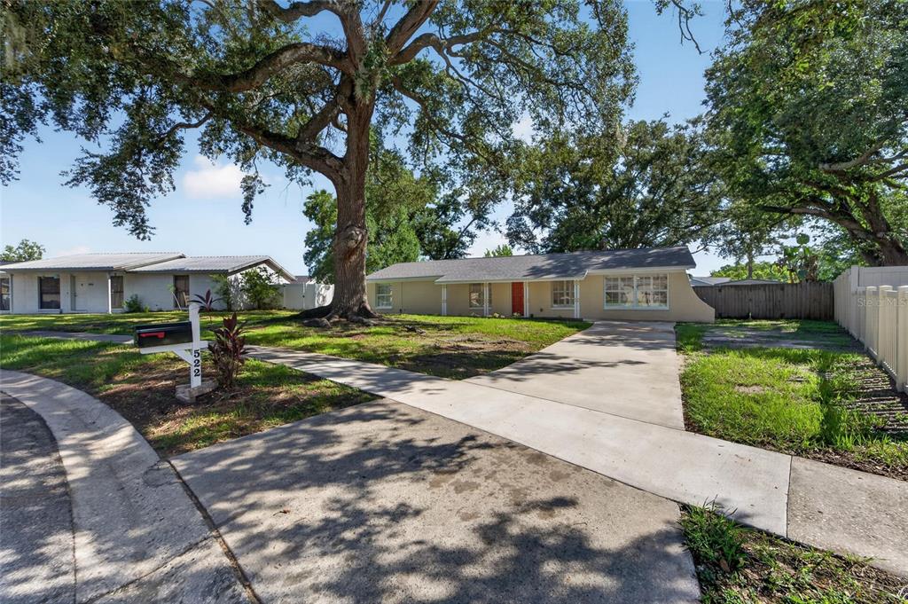A single-story house with a beige exterior, a dark roof, and a large front tree — 522 HIGHVIEW CIRCLE N, BRANDON, FL