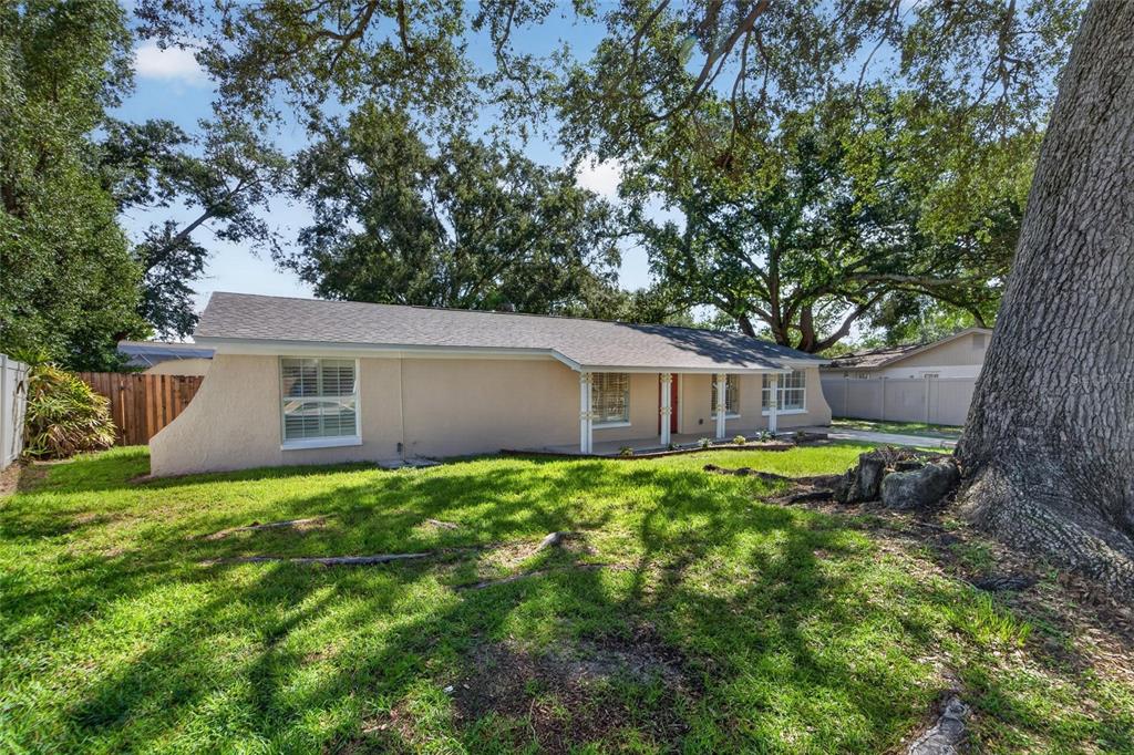 A single-story house with a beige stucco exterior, a covered porch, and large oak trees — 522 HIGHVIEW CIRCLE N, BRANDON, FL