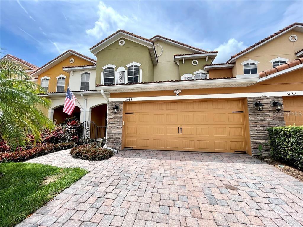 A two-story townhouse exterior features a tan garage, stone accents, and a paved driveway — 5083 FIORELLA LANE, SANFORD, FL
