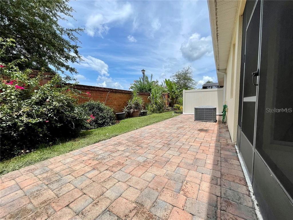 A paved patio area sits beside a house with a brick wall and landscaping — 5083 FIORELLA LANE, SANFORD, FL