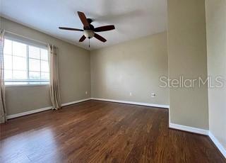 An empty bedroom features wood-look flooring, beige walls, a ceiling fan, and a window with curtains — 5083 FIORELLA LANE, SANFORD, FL