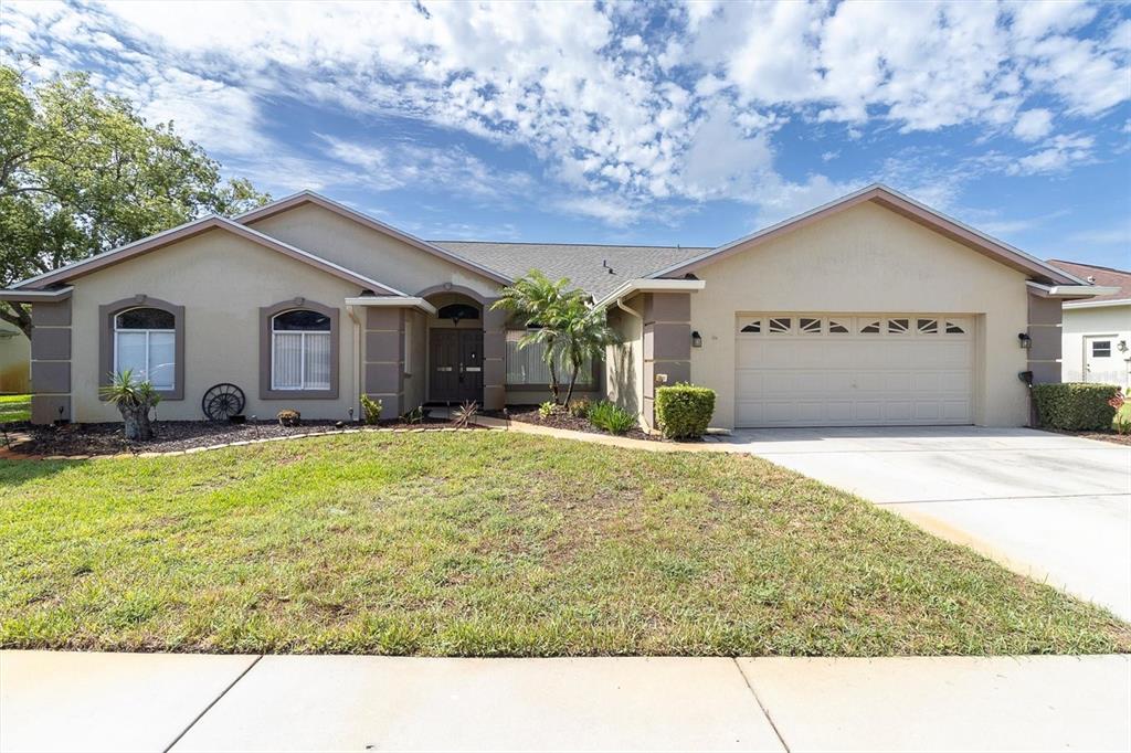 A single-story house with a beige stucco exterior, a two-car garage, and a front lawn — 8303 CORAL CREEK LOOP, HUDSON, FL