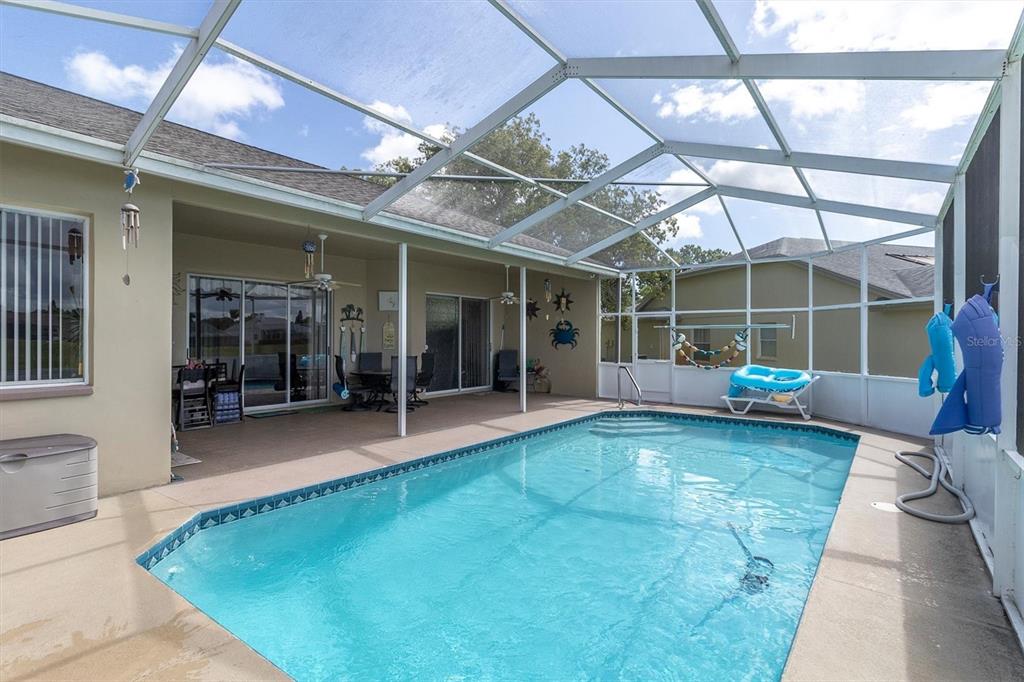 A screened-in swimming pool with a covered patio area and outdoor furniture — 8303 CORAL CREEK LOOP, HUDSON, FL