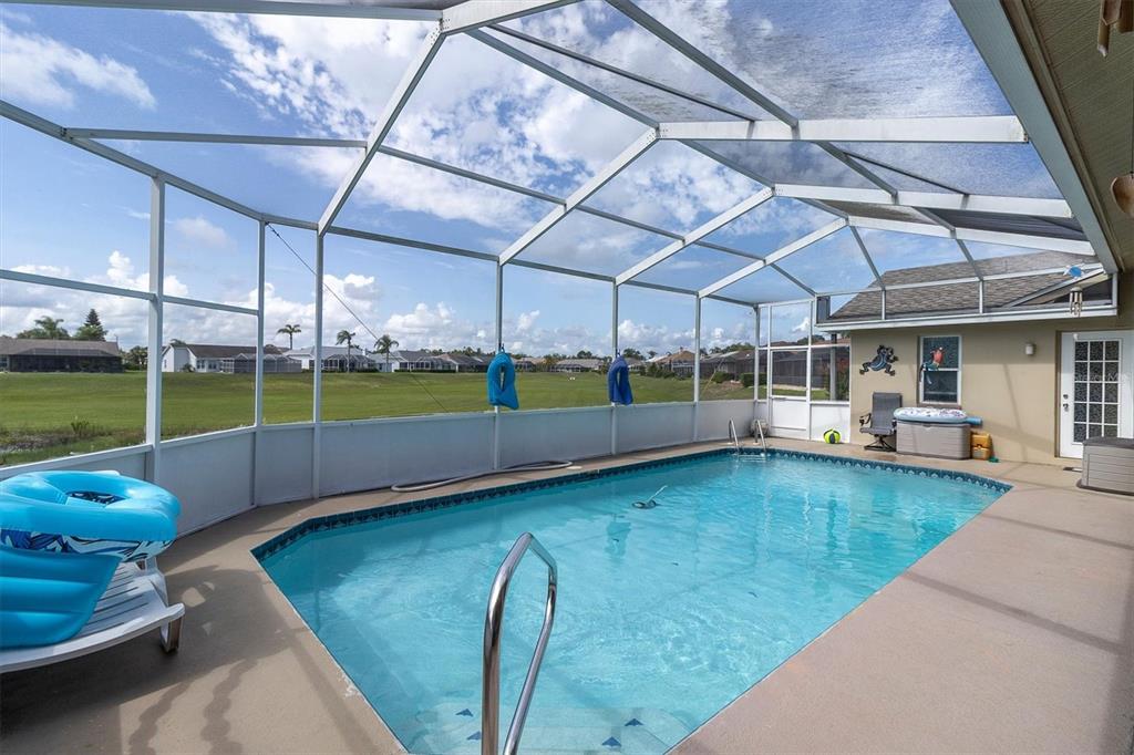 A screened-in swimming pool with a concrete deck overlooks a grassy field under a sky — 8303 CORAL CREEK LOOP, HUDSON, FL