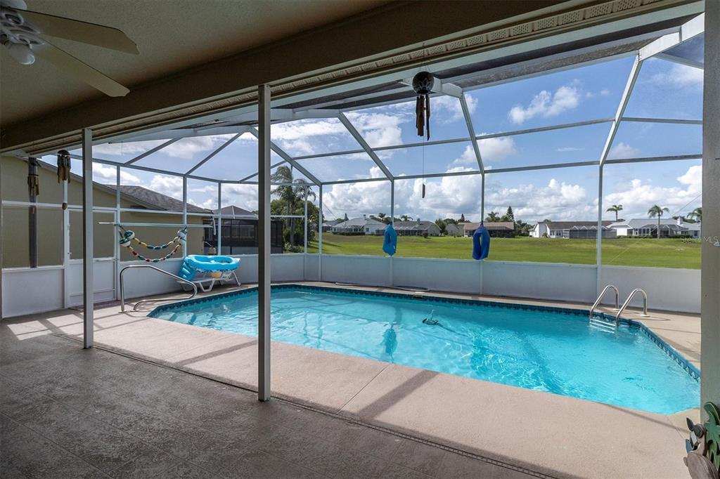 A screened-in lanai features a rectangular swimming pool overlooking a grassy field and neighborhood homes — 8303 CORAL CREEK LOOP, HUDSON, FL
