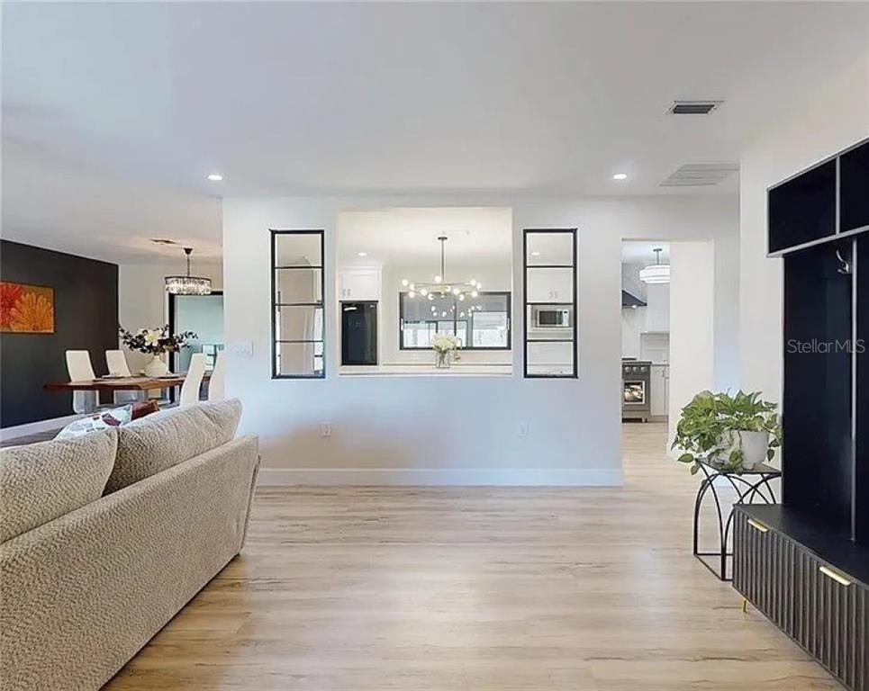 A living room with light wood floors looks through a pass-through window into a kitchen — 7699 NW 56TH PLACE, OCALA, FL