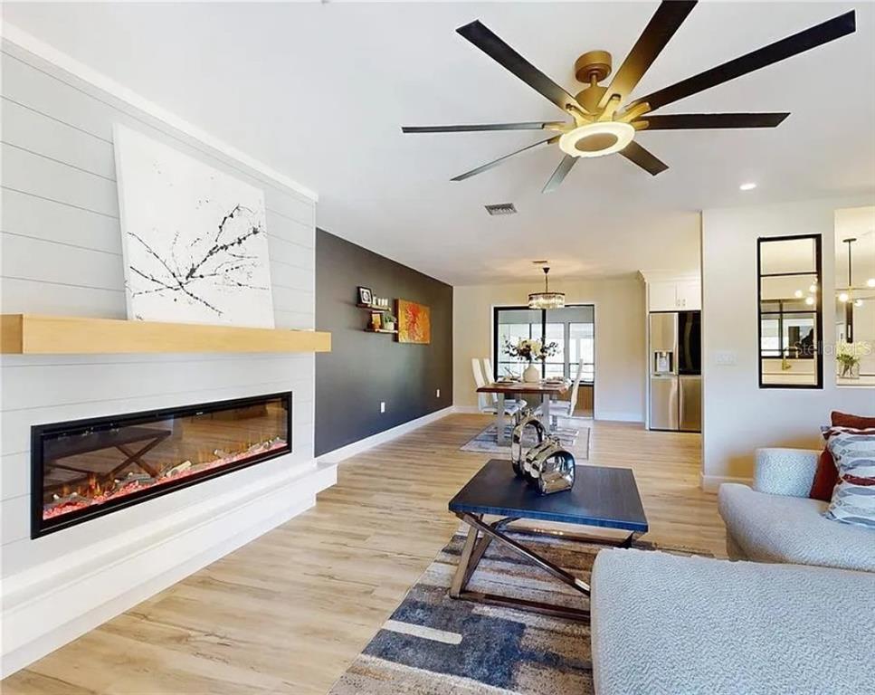 A living room features a linear fireplace, shiplap wall, dark accent wall, and ceiling fan — 7699 NW 56TH PLACE, OCALA, FL