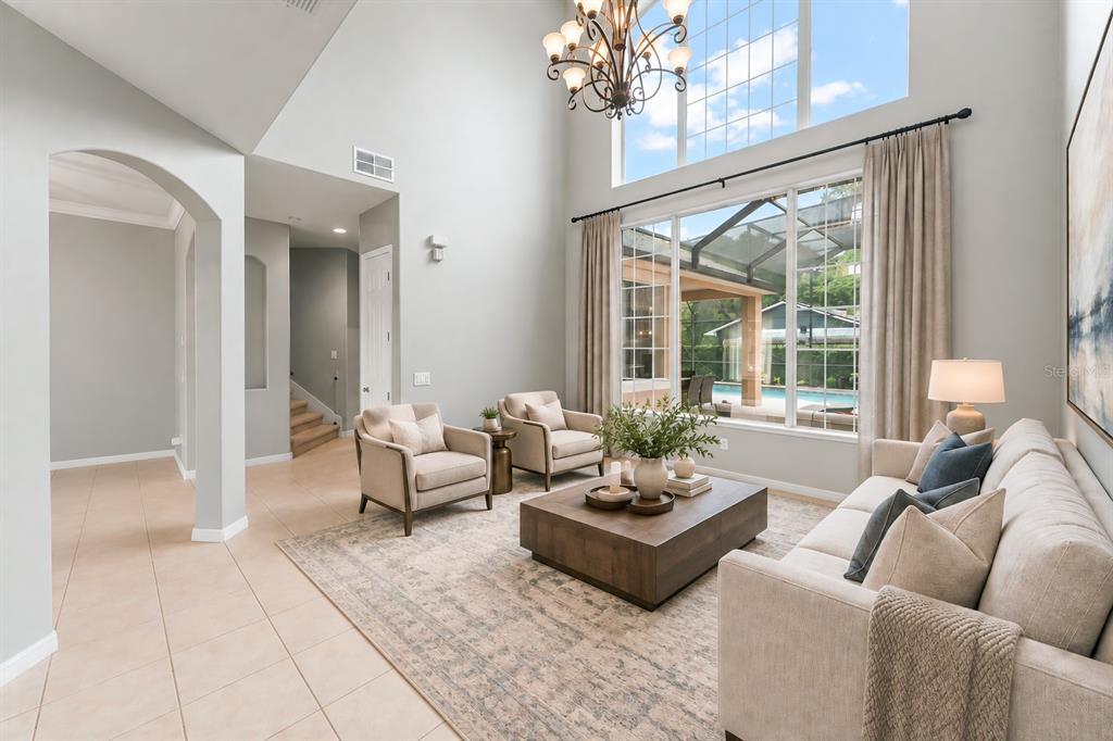 A high-ceilinged living room features tile flooring, two gray sofas, and large windows overlooking a pool — 14411 HAMPSHIRE BAY CIRCLE, WINTER GARDEN, FL