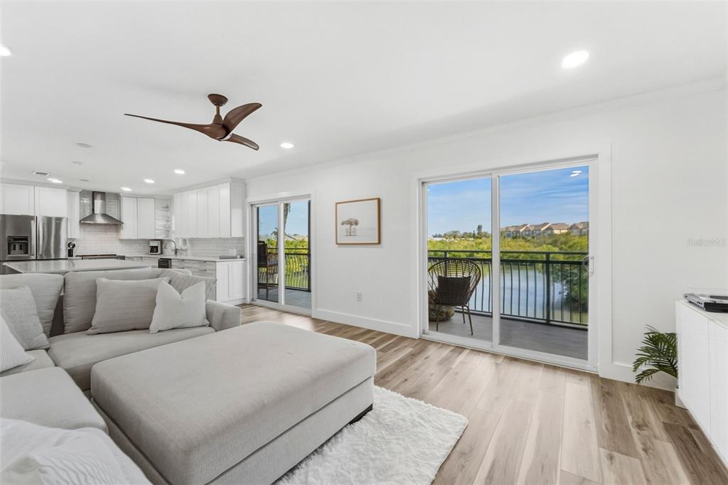 A living room with light wood floors, a sectional sofa, and sliding doors overlooking water — 8806 BAY POINTE DRIVE UNIT 206, TAMPA, FL