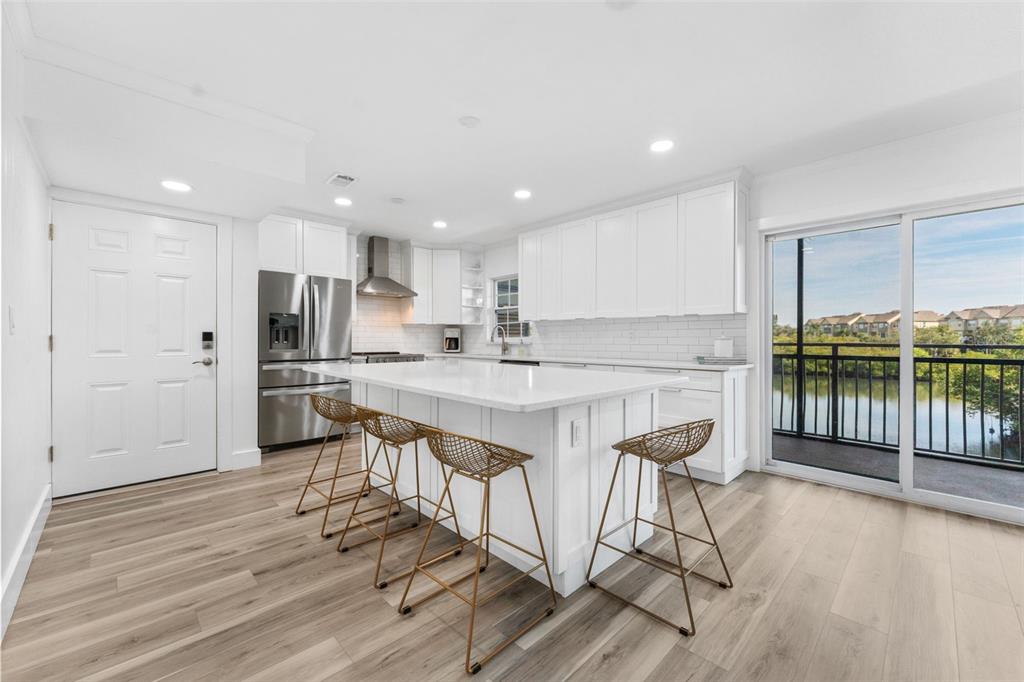 A modern white kitchen features a large island with gold barstools and a balcony view — 8806 BAY POINTE DRIVE UNIT 206, TAMPA, FL