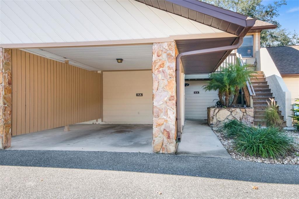 A carport with a stone pillar sits next to an outdoor staircase leading to a residence — 95 E HARTFORD STREET UNIT 7A, HERNANDO, FL