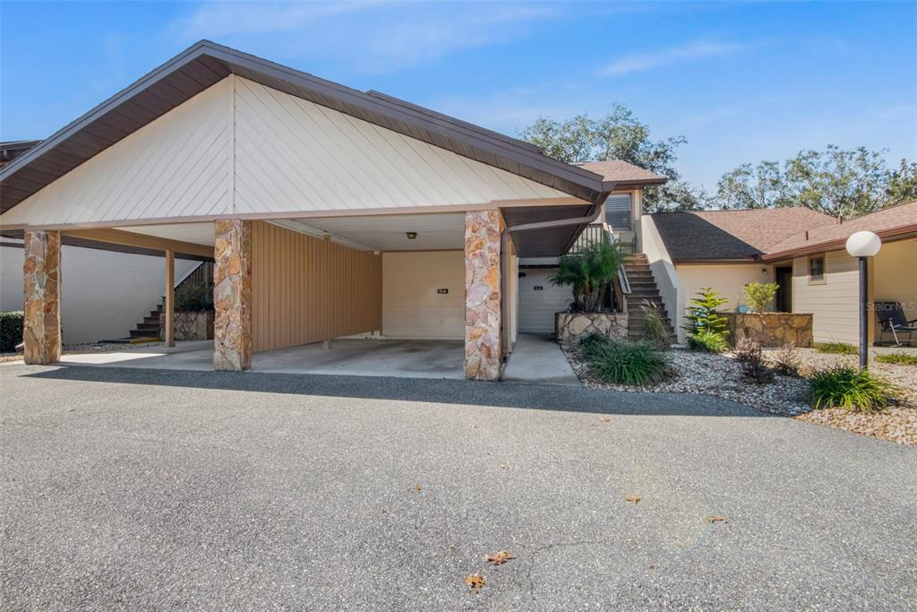 A covered carport with stone pillars sits in front of a multi-level residential building — 95 E HARTFORD STREET UNIT 7A, HERNANDO, FL