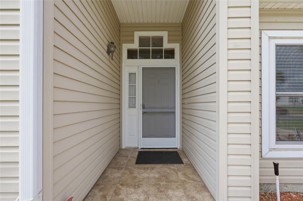 A covered entryway features beige vinyl siding, a tiled floor, and a grey front door — 5350 ASTOR STREET, LEESBURG, FL