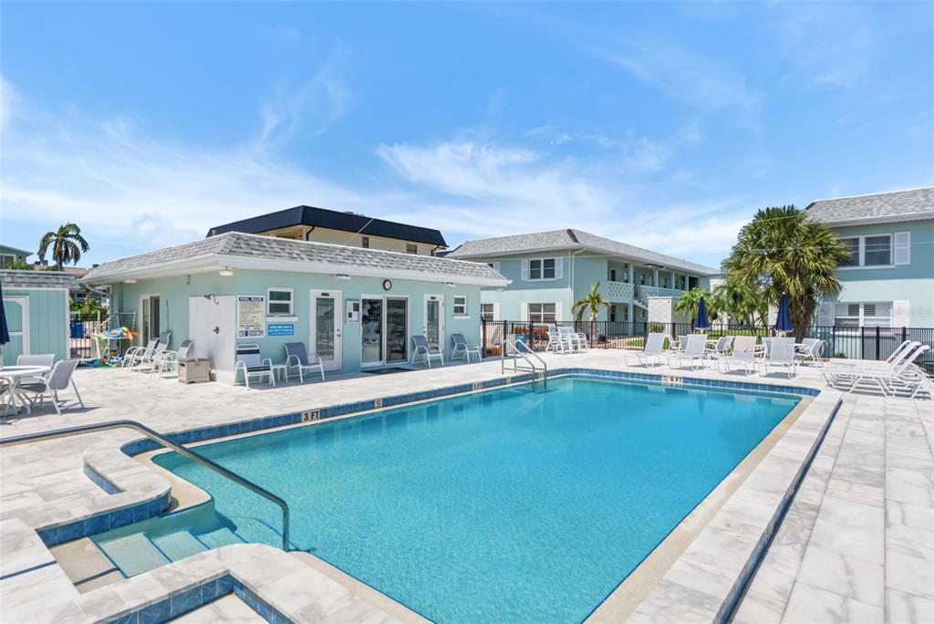 An aerial view shows a sandy beach with thatched-roof structures, umbrellas, and nearby coastal buildings — 611 GULF DRIVE N UNIT C27, BRADENTON BEACH, FL