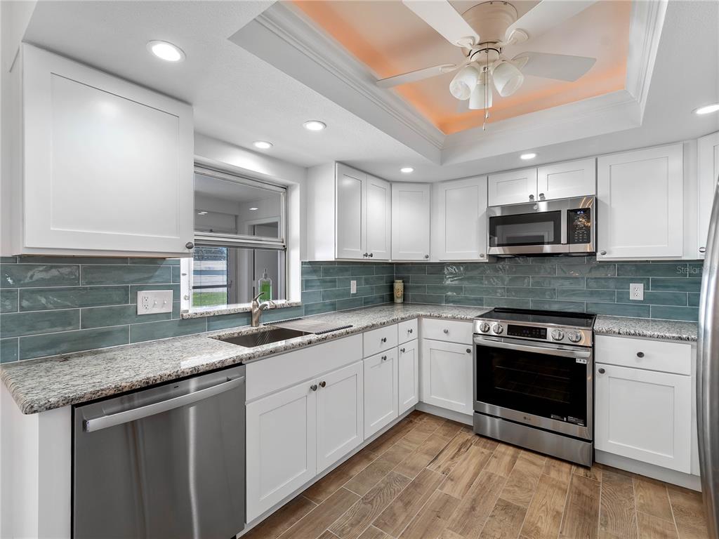A kitchen with white cabinets, granite countertops, blue subway tile backsplash, and stainless steel appliances — 52 CIRCLEWOOD DRIVE UNIT A1-2, VENICE, FL