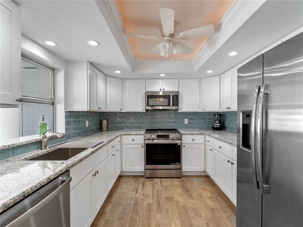 A kitchen with white cabinets, stainless steel appliances, granite countertops, and a blue tile backsplash — 52 CIRCLEWOOD DRIVE UNIT A1-2, VENICE, FL