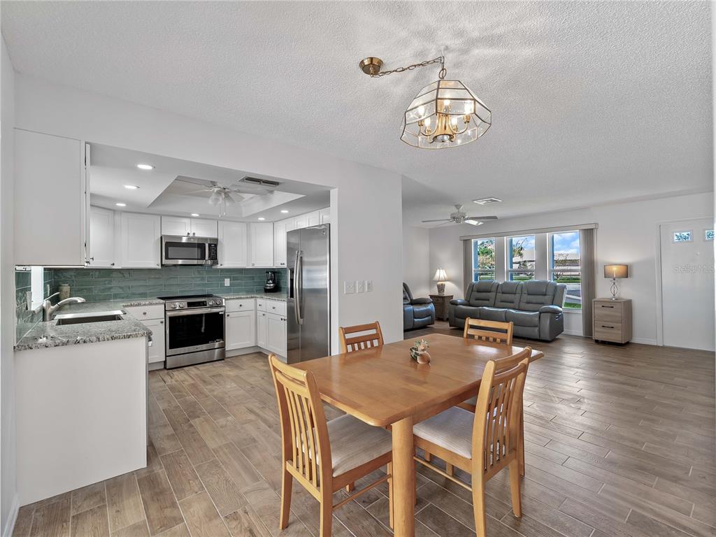 An open-concept kitchen and dining area with white cabinets, stainless appliances, and wood-look tile flooring — 52 CIRCLEWOOD DRIVE UNIT A1-2, VENICE, FL