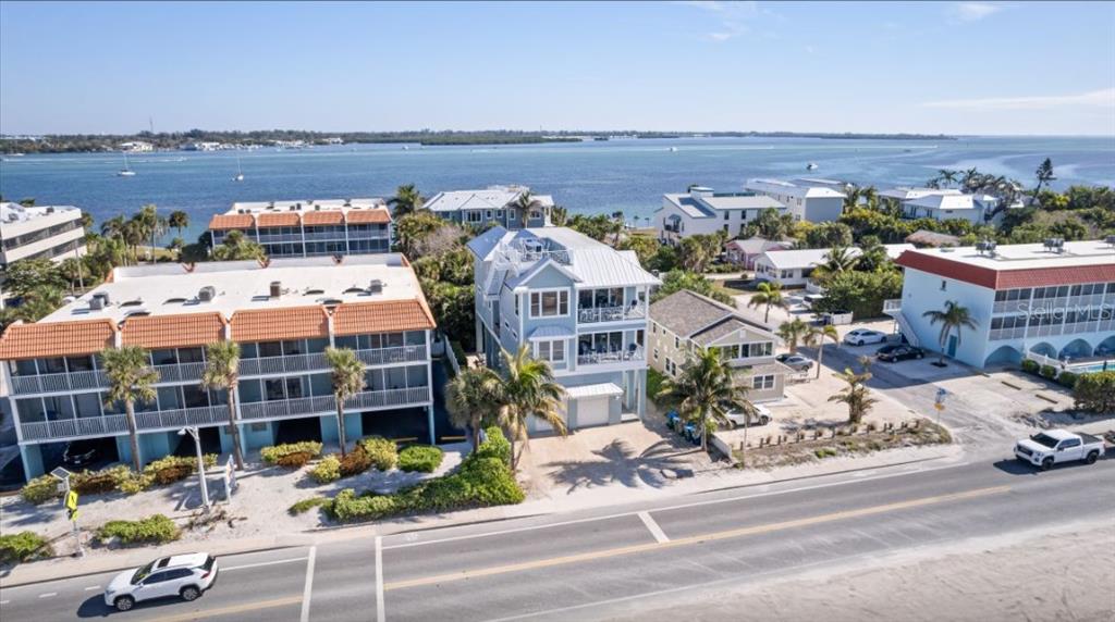 An aerial view shows a multi-story blue house situated between apartment buildings near the water — 903 GULF DRIVE S, BRADENTON BEACH, FL