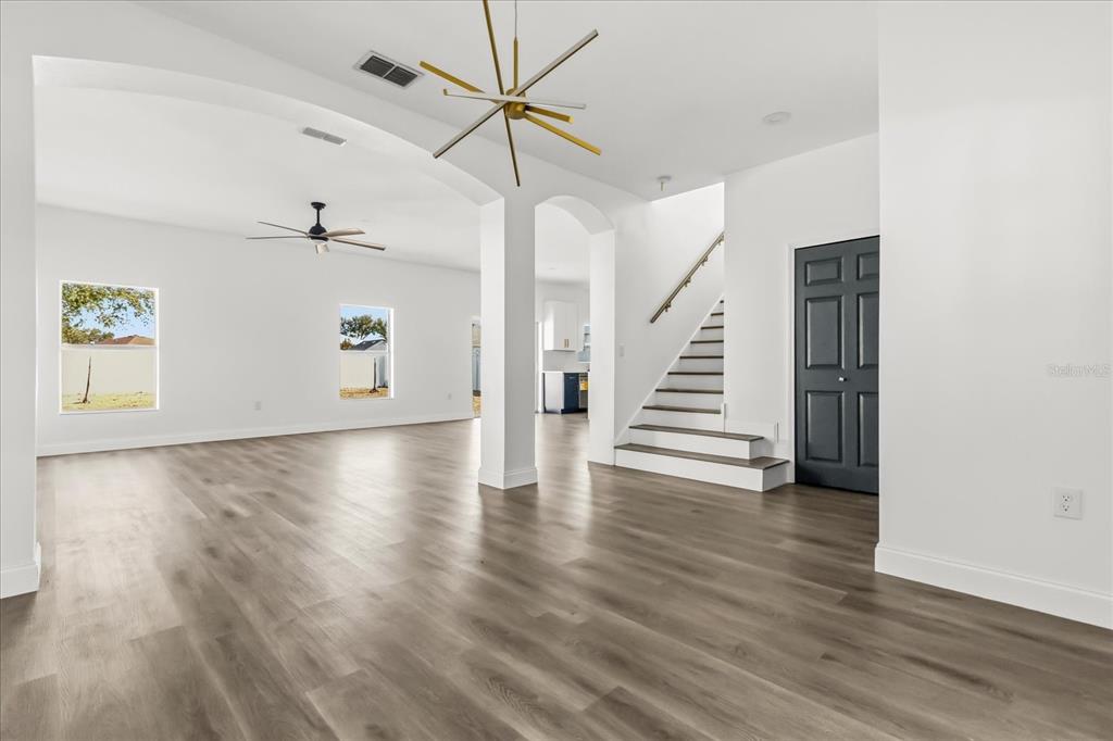 An open-concept living area features light wood-look flooring, a modern chandelier, and a staircase — 15663 DURANGO CIRCLE, BROOKSVILLE, FL