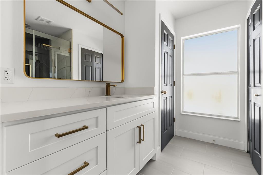 A modern bathroom features a white vanity with gold hardware, a gold-framed mirror, and tile flooring — 15663 DURANGO CIRCLE, BROOKSVILLE, FL
