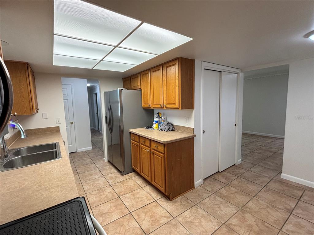 A kitchen features wood cabinets, stainless steel appliances, tan countertops, and tiled flooring — 103 BILSDALE COURT, LONGWOOD, FL