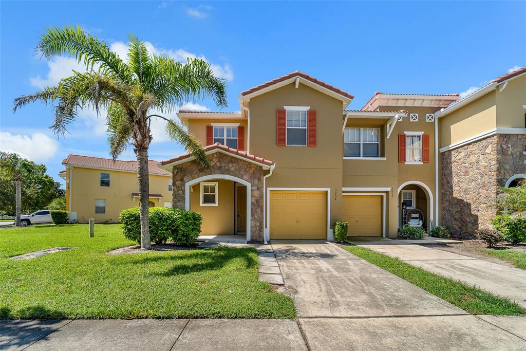 A two-story townhouse with a tan stucco exterior, stone accents, and two attached garages — 3064 SEAVIEW CASTLE DRIVE, KISSIMMEE, FL