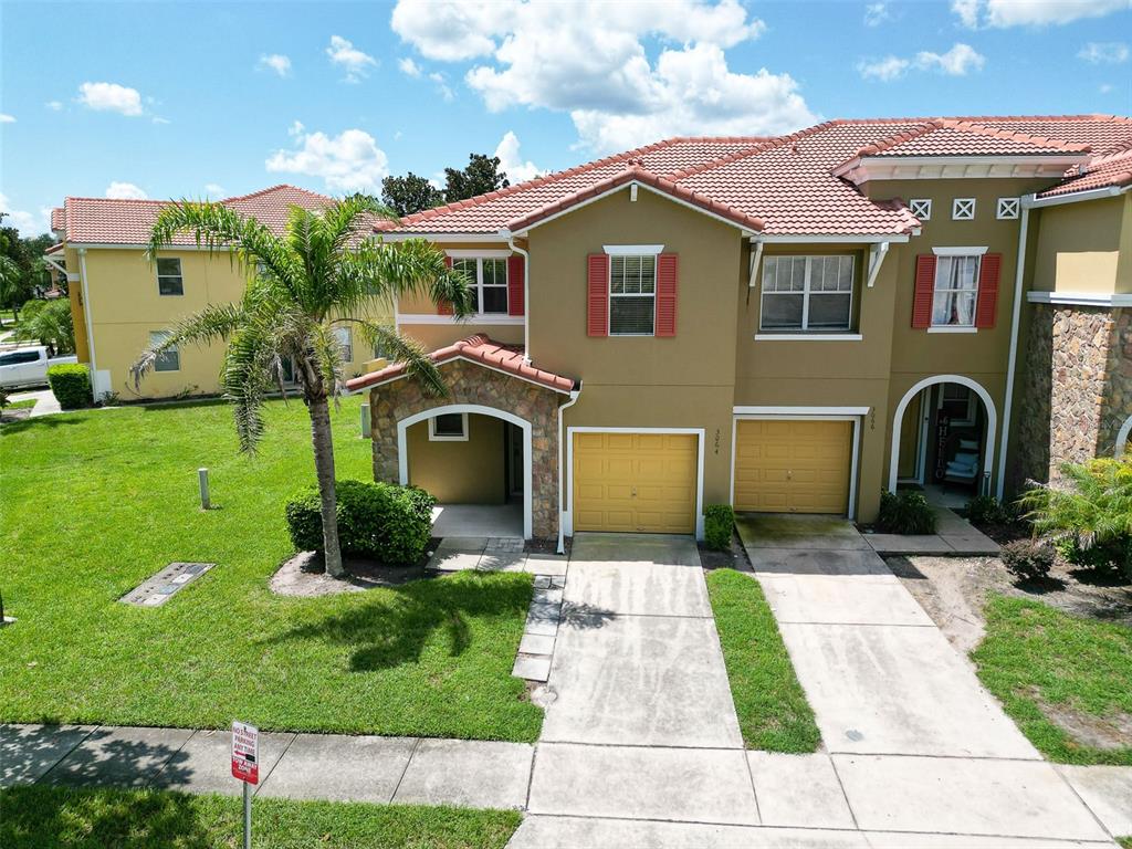 An exterior view of a two-story townhouse with a tan stucco facade and two garages — 3064 SEAVIEW CASTLE DRIVE, KISSIMMEE, FL