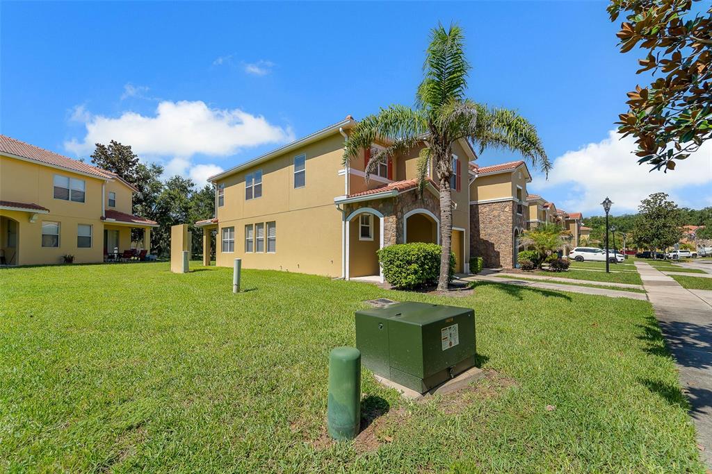 A two-story tan stucco townhouse with a palm tree and green utility boxes in front — 3064 SEAVIEW CASTLE DRIVE, KISSIMMEE, FL