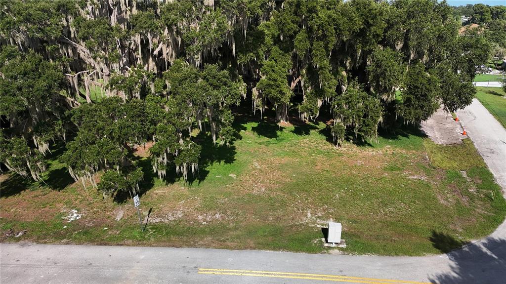 An aerial view shows a vacant, grassy corner lot shaded by large, moss-covered oak trees — LAKESIDE DRIVE, YALAHA, FL