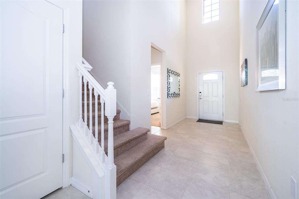 An entryway features a carpeted staircase with a white railing, tile flooring, and high ceilings — 1690 LIMA AVENUE, KISSIMMEE, FL