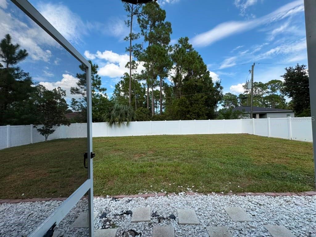A fenced backyard with a grassy lawn, white gravel patio, and tall pine trees — 2743 SOMERSET, PALM BAY, FL